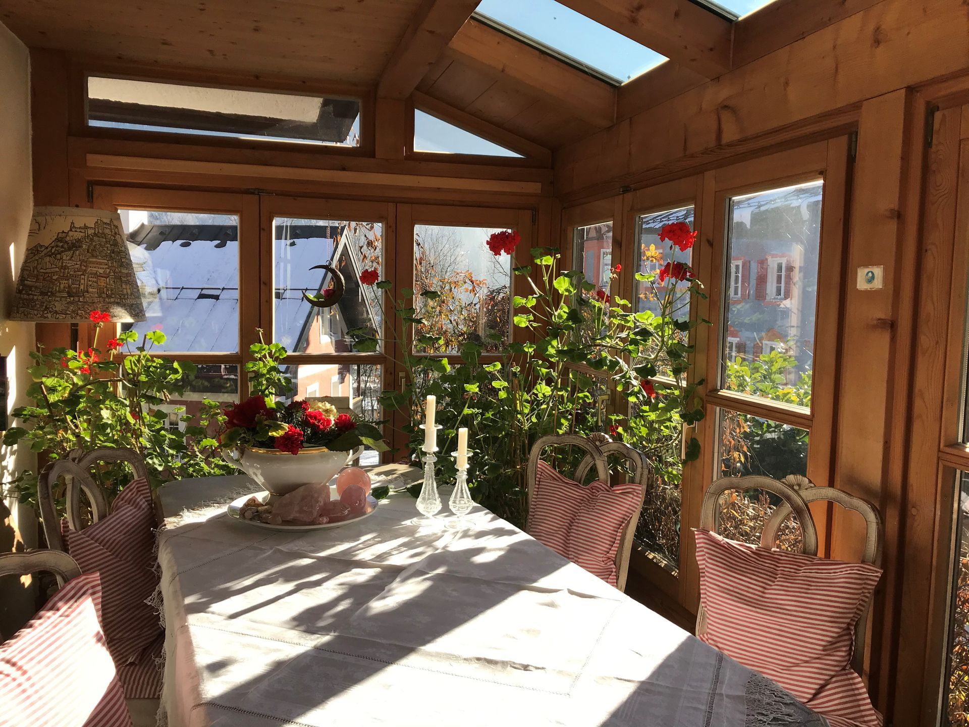 Wintergarten mit gedecktem Esstisch, umgeben von Pflanzen und Fenstern.