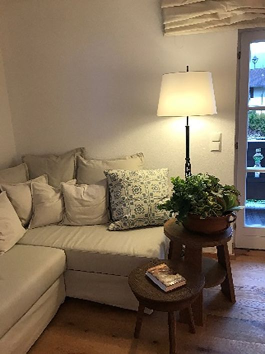 Gemütliche Ecke mit cremefarbenem Sofa, Lampe, Holztisch und Pflanze neben einer Tür.