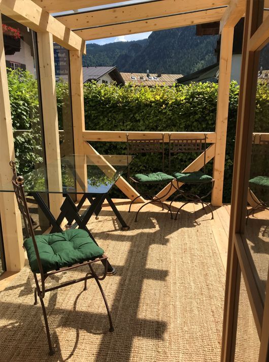 Sitzbereich im Freien mit Tisch, Stühlen, grünen Kissen, Holzrahmen und Bergblick.