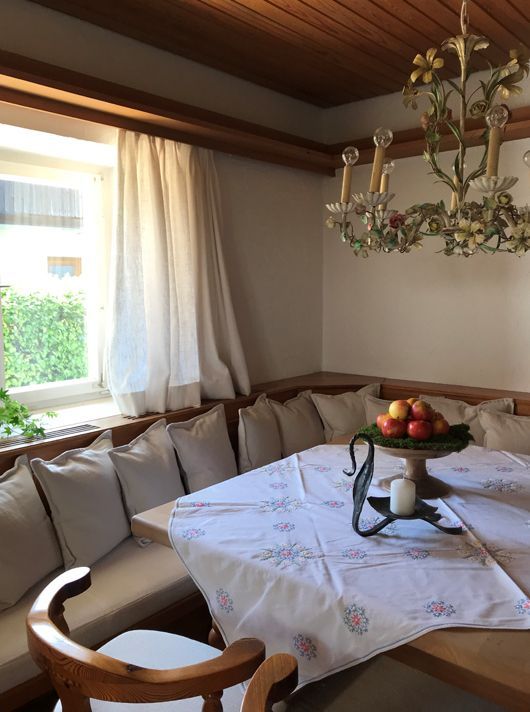 Gemütliche Essecke mit Fenster, eingebauter Bank, gedecktem Tisch und floralem Kronleuchter.