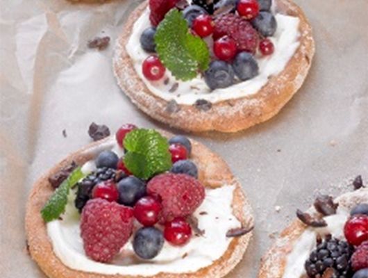 Mini-Obstpizzas mit Beeren und Sahne auf Backpapier.