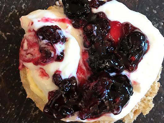 Nahaufnahme eines Gebäcks mit weißer Sahne und dunkler Brombeermarmelade.