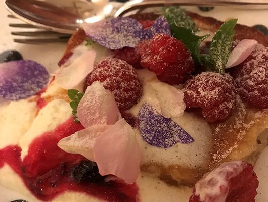 Nahaufnahme eines Desserts mit Himbeeren, Blaubeeren, essbaren Blüten und Sahne.