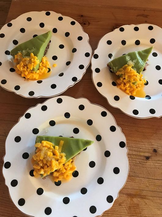 Drei Teller mit Punkten, jeder mit einem Stück grünem Kuchen und gelbem Belag, auf einem Holztisch.