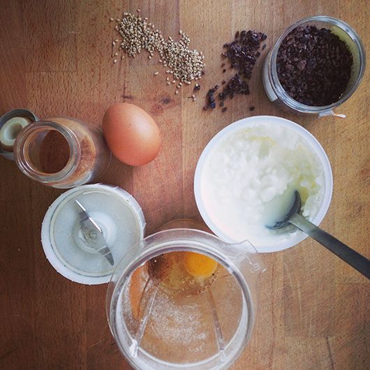 Zutaten für ein Rezept auf einer Holzoberfläche: Ei, Sesamsamen, Schokolade, Kokosöl und ein Mixer.