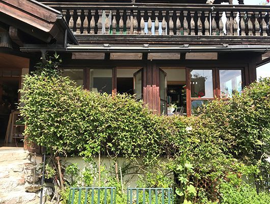 Biohotel Kurz mit Fenstern und einem Balkon, teilweise verdeckt durch grüne Sträucher.