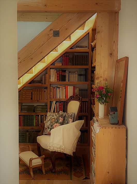 Gemütliche Leseecke unter der Treppe mit Bücherregalen, Sessel, kleinem Stuhl und Holzakzenten.