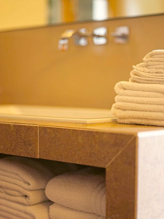 Gestapelte weiße Handtücher in einem Badezimmer mit eingebautem Regal und modernen Chromarmaturen.