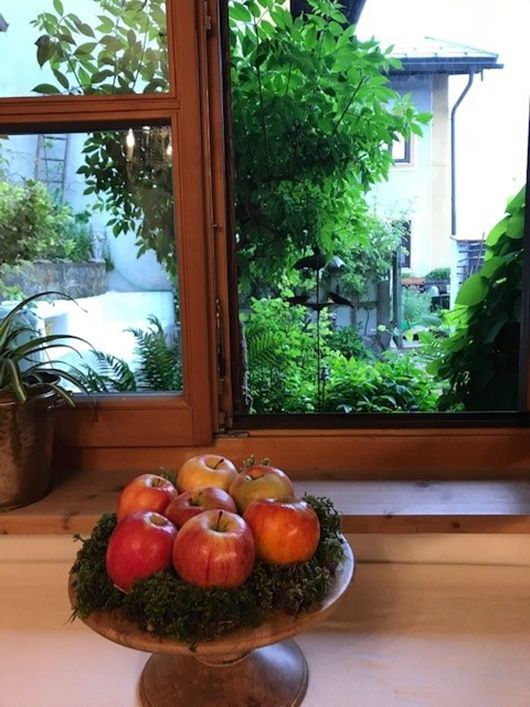 Äpfel auf einem Holzständer vor einem offenen Fenster mit Blick ins Grüne.