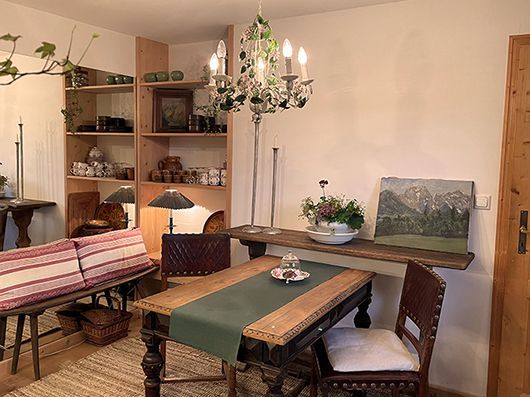 Esszimmer mit Holztisch, Stühlen, Regal mit Dekor, Bank mit Kissen und einem Kronleuchter.