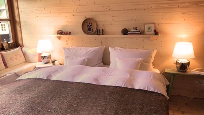 Gemütliches Schlafzimmer mit Holzwänden, Bett, Lampen und einem kleinen Sofa am Fenster.