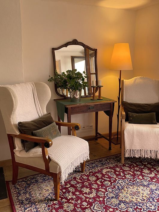 Gemütliche Wohnzimmerecke mit zwei Sesseln, einem Teppich, einem Tisch mit Spiegel und Stehlampe.