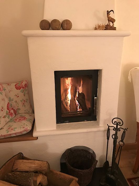 Weißer Kamin mit brennendem Feuer. Holzstapel, Werkzeuge und Dekorationsgegenstände in der Nähe.