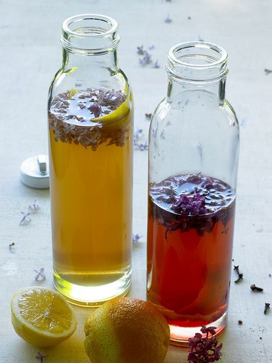 Zwei Glasflaschen gefüllt mit Fliedergetränken; Zitronen stehen daneben.