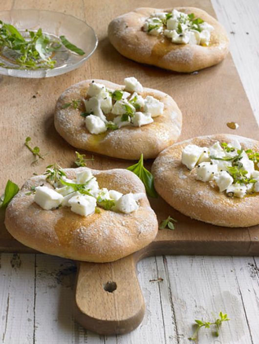 Focaccia mit Feta, Kräutern und Olivenöl auf einem Holzschneidebrett.