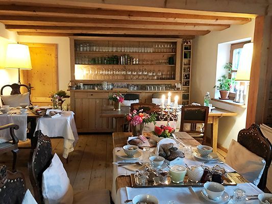 Frühstückstisch in einem gemütlichen Raum mit Holzbalken und einem Schrank voller Gläser.