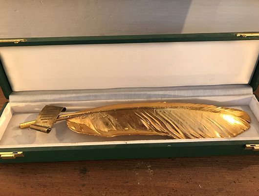 Goldener Stift in Federform in einer grün-weißen Präsentationsbox.