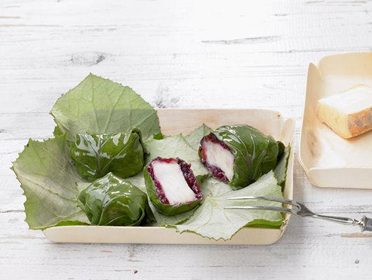 Nahaufnahme des Essens: In Blätter gewickeltes Mochi mit roter Füllung in einer Servierschale.