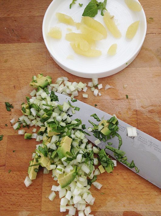 Gehackte Avocado, Zwiebel und Koriander auf einem Holzschneidebrett mit einem Messer.