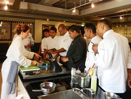 Gabi Kurz demonstriert einer Gruppe in einer gut beleuchteten Küche Kochtechniken.