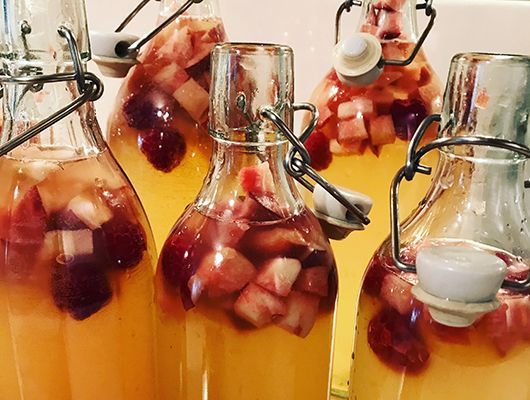 Flaschen gefüllt mit gelber Flüssigkeit und Früchten, mit Metall- und Keramikverschlüssen.