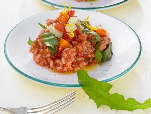 Teller Tomatenrisotto mit Gemüse und Löwenzahn.