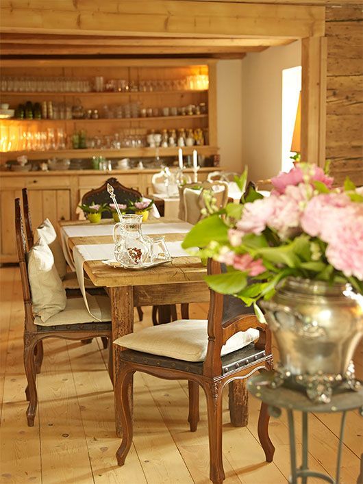 Für eine Mahlzeit gedeckter Esstisch aus Holz, im Hintergrund Blumenarrangement und Vitrine.