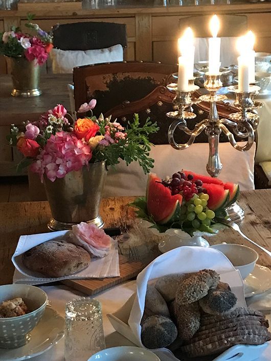 Gedeckter Tisch für ein Essen mit Blumen, Obst, Brot und brennenden Kerzen in antikem Ambiente.