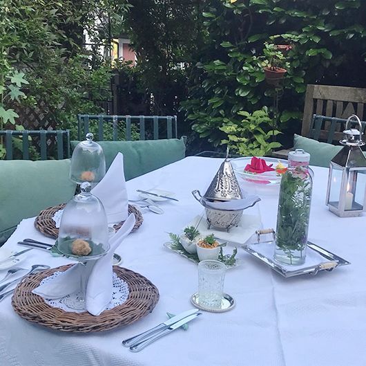 Tischdekoration im Freien mit weißer Tischdecke, dekorativen Tafelaufsätzen und Grünpflanzen.