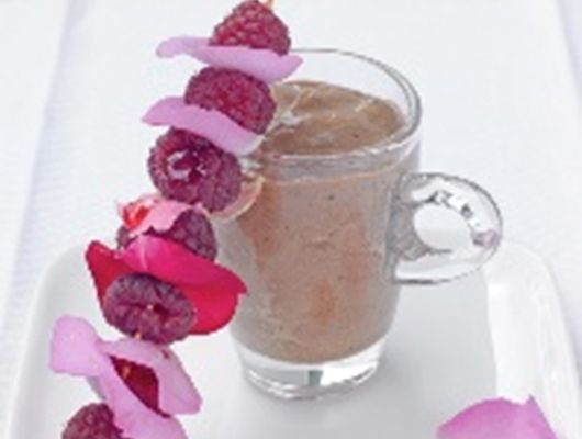 Glas mit einem braunen Smoothie, garniert mit einem Spieß aus Himbeeren und Rosenblättern.
