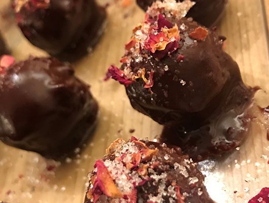 Rosenpralinen, garniert mit Rosenblättern und Zucker auf einer Holzoberfläche.