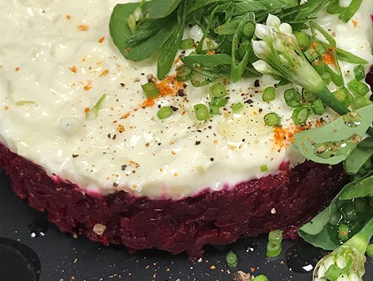 Rote-Bete-Tartar mit cremigem weißen Belag, grüner Garnitur und schwarzem Pfeffer.