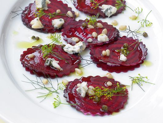 Rote-Bete-Carpaccio mit Blauschimmelkäse, Pinienkernen, Kapern und Dill auf einem weißen Teller.