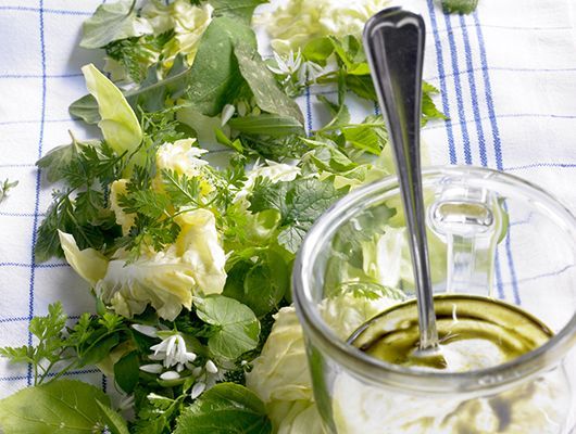 Salatgrün und Dressing in einem Glasgefäß mit einem Löffel auf einem karierten Tuch.
