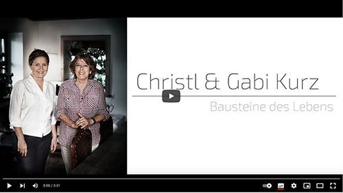 Christl und Gabi Kurz, stehen neben einer Titelkarte mit der Aufschrift „Bausteine ​​des Lebens“.