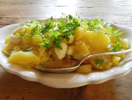 Kartoffelsalat in weißer Schale, garniert mit Vogelmiere, auf Holztisch.