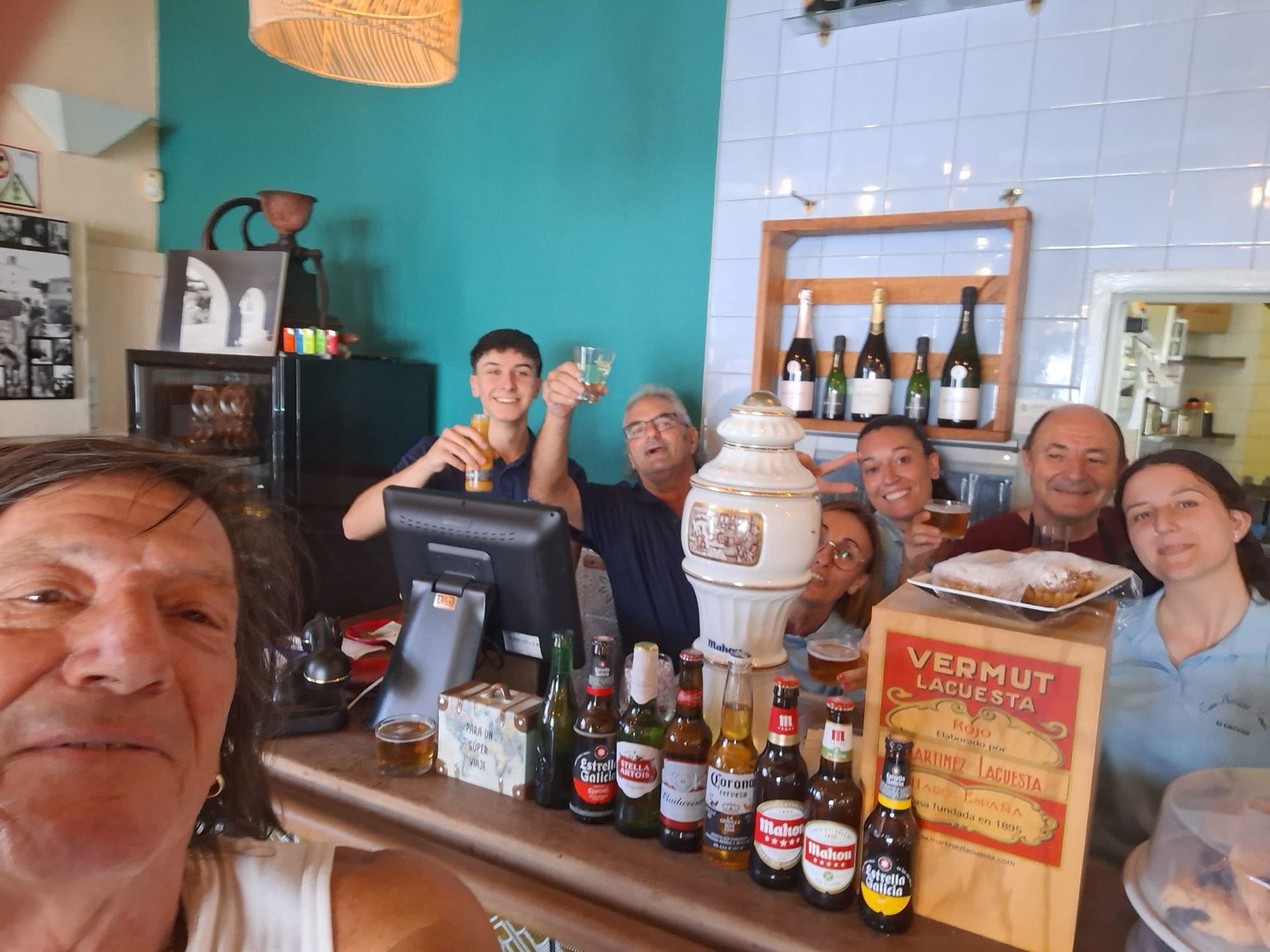Gente en un bar, sonriendo y alzando sus copas. Un hombre se toma una selfi. Se ven varias cervezas y botellas.