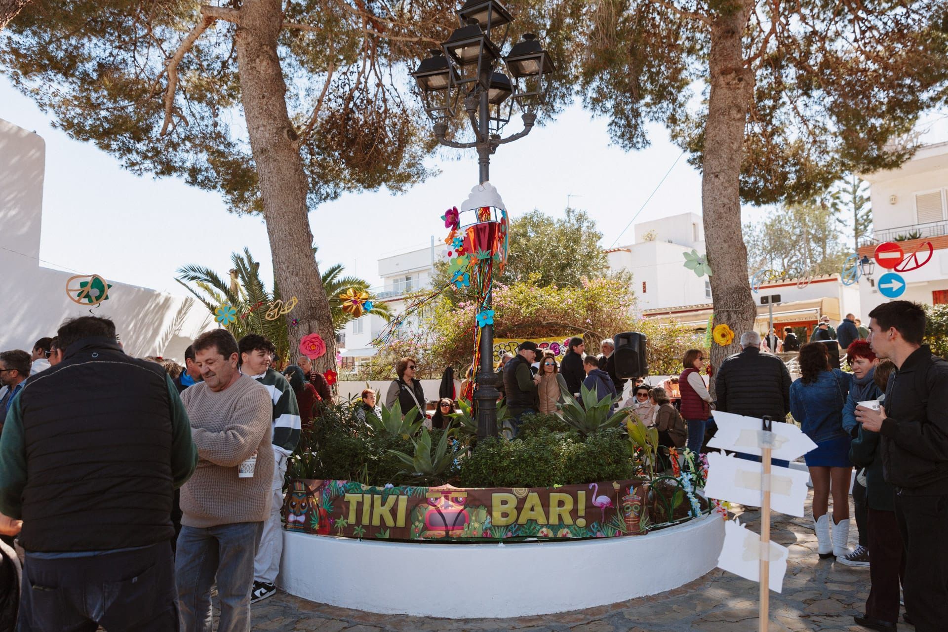 La gente se reúne en un bar Tiki con decoraciones coloridas bajo los árboles. Un sol radiante y un ambiente alegre.