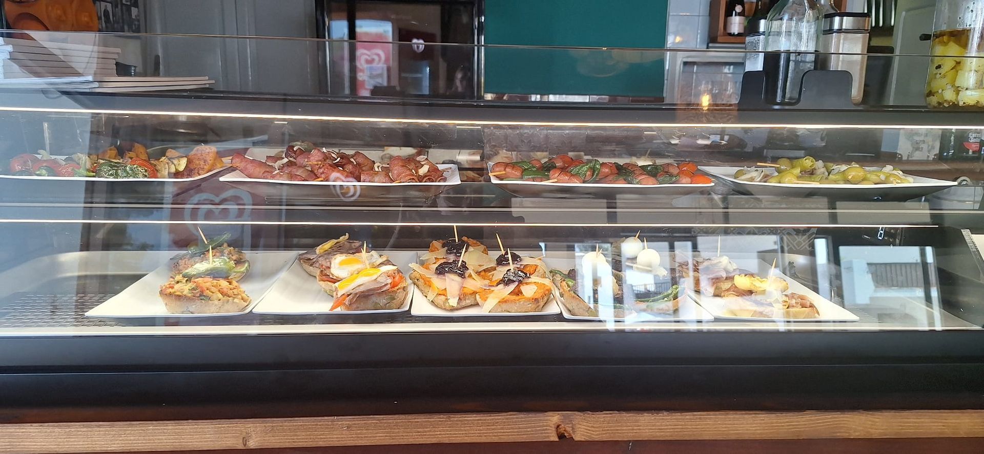 Una vitrina de cristal en un restaurante contiene pequeños platos de comida. Los platos están dispuestos en estantes, con varios platos a la vista.