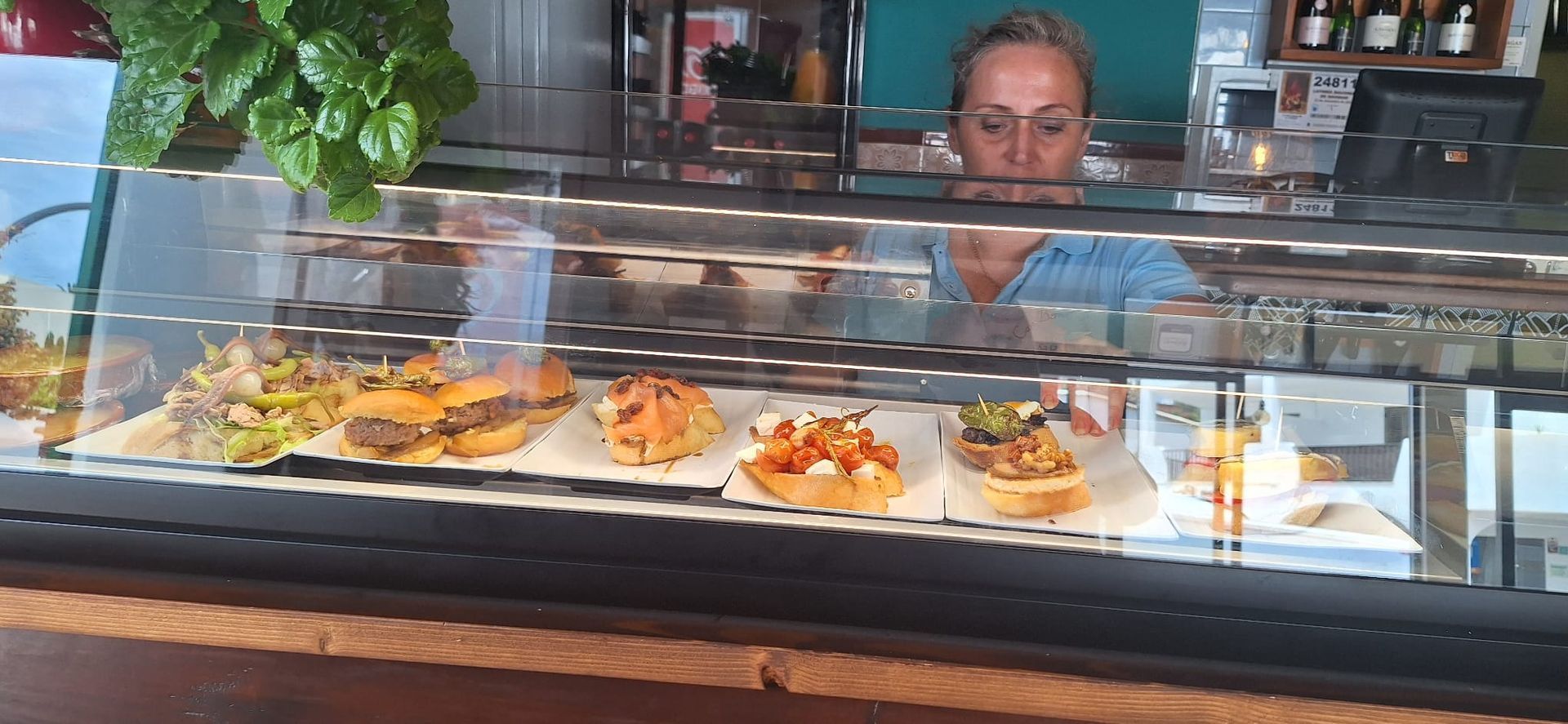 Una persona está detrás de una vitrina llena de diversos alimentos. Mira a la cámara.