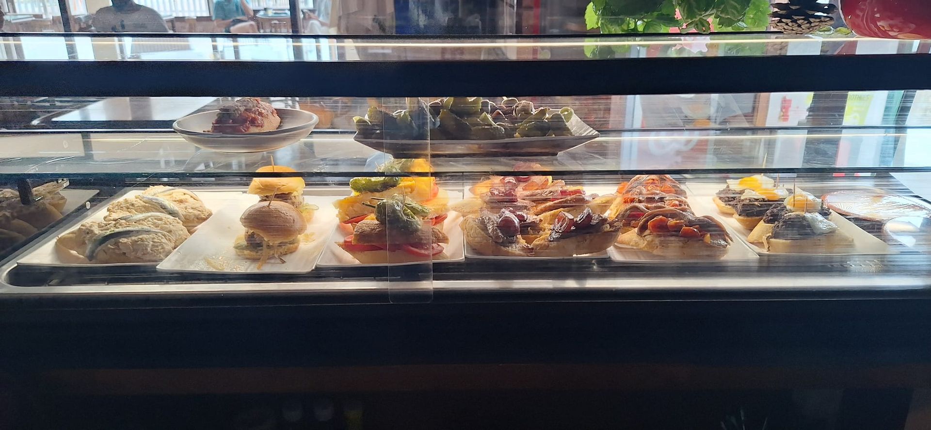 Vitrina llena de diversos alimentos preparados, posiblemente sándwiches o aperitivos, en un restaurante o cafetería.