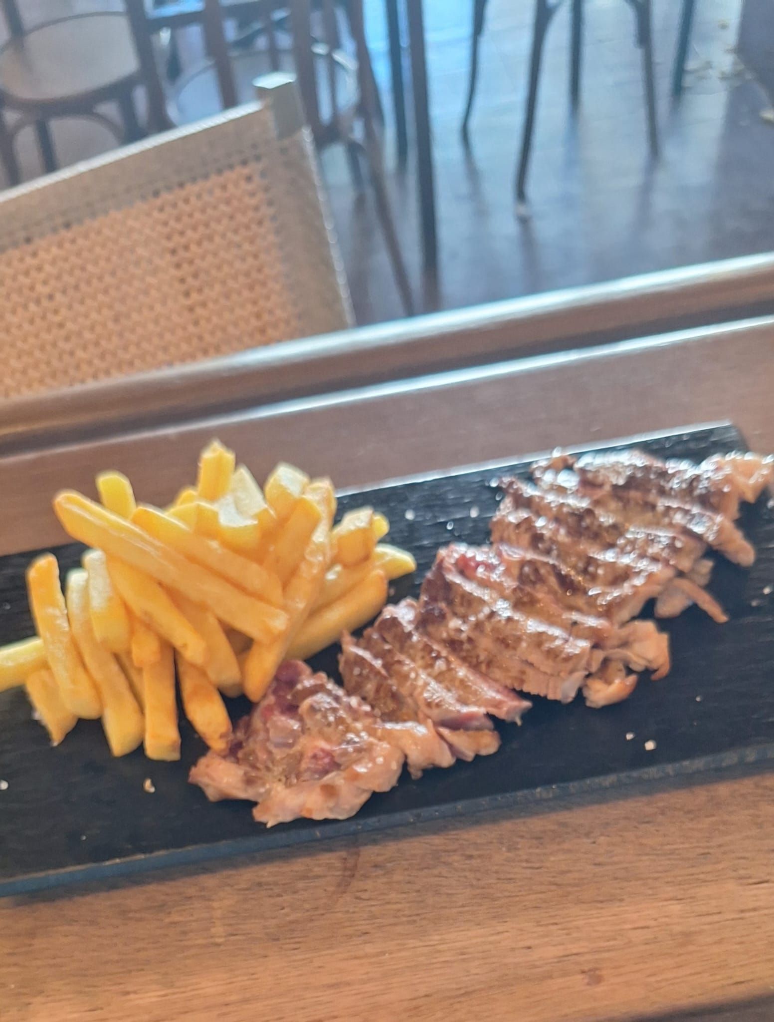 Bistec a la parrilla y papas fritas en un plato rectangular negro, servido en un restaurante.