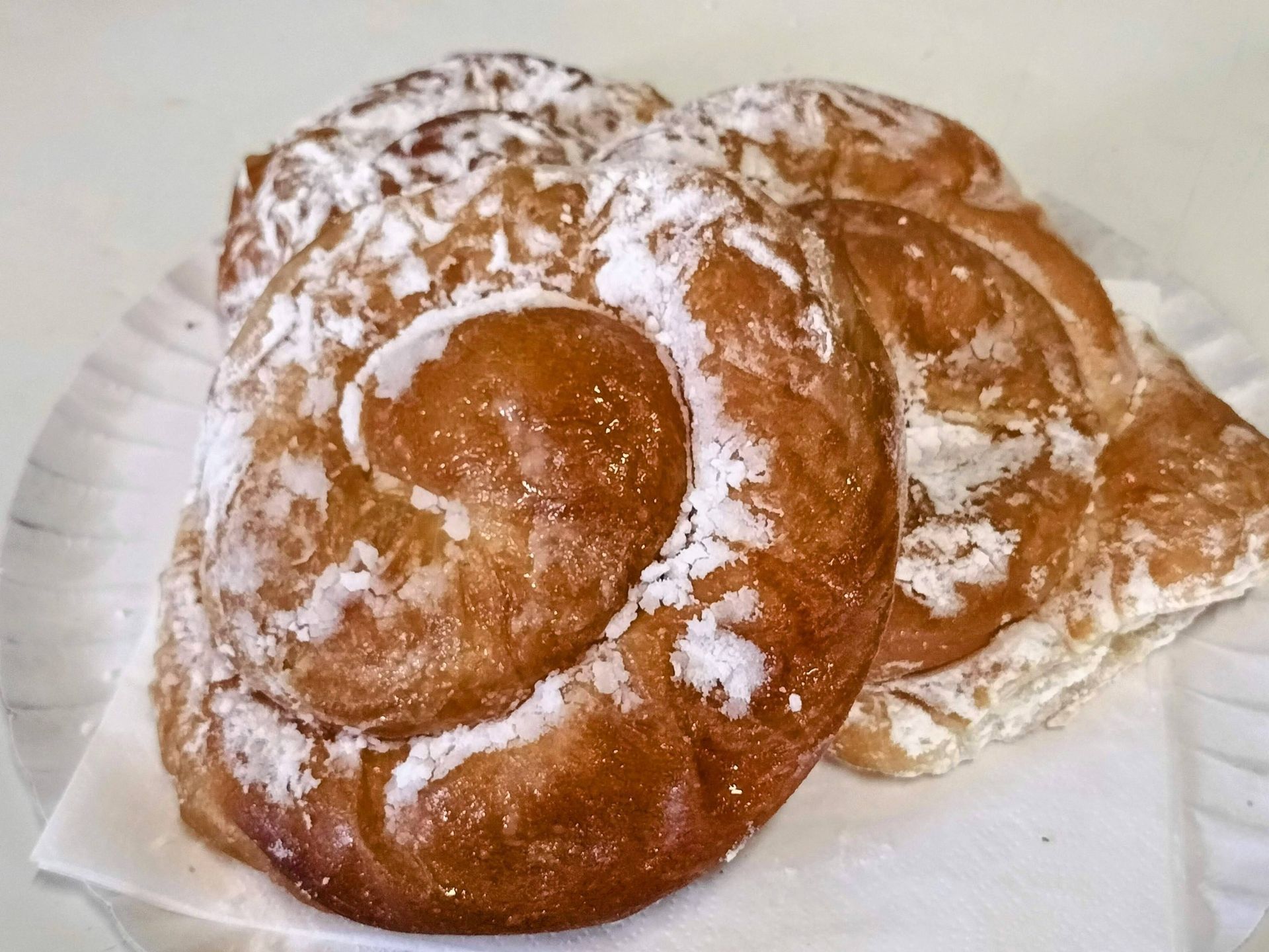 Tres pasteles glaseados y espolvoreados con azúcar glas en un plato de papel. Los pasteles tienen forma de espiral.