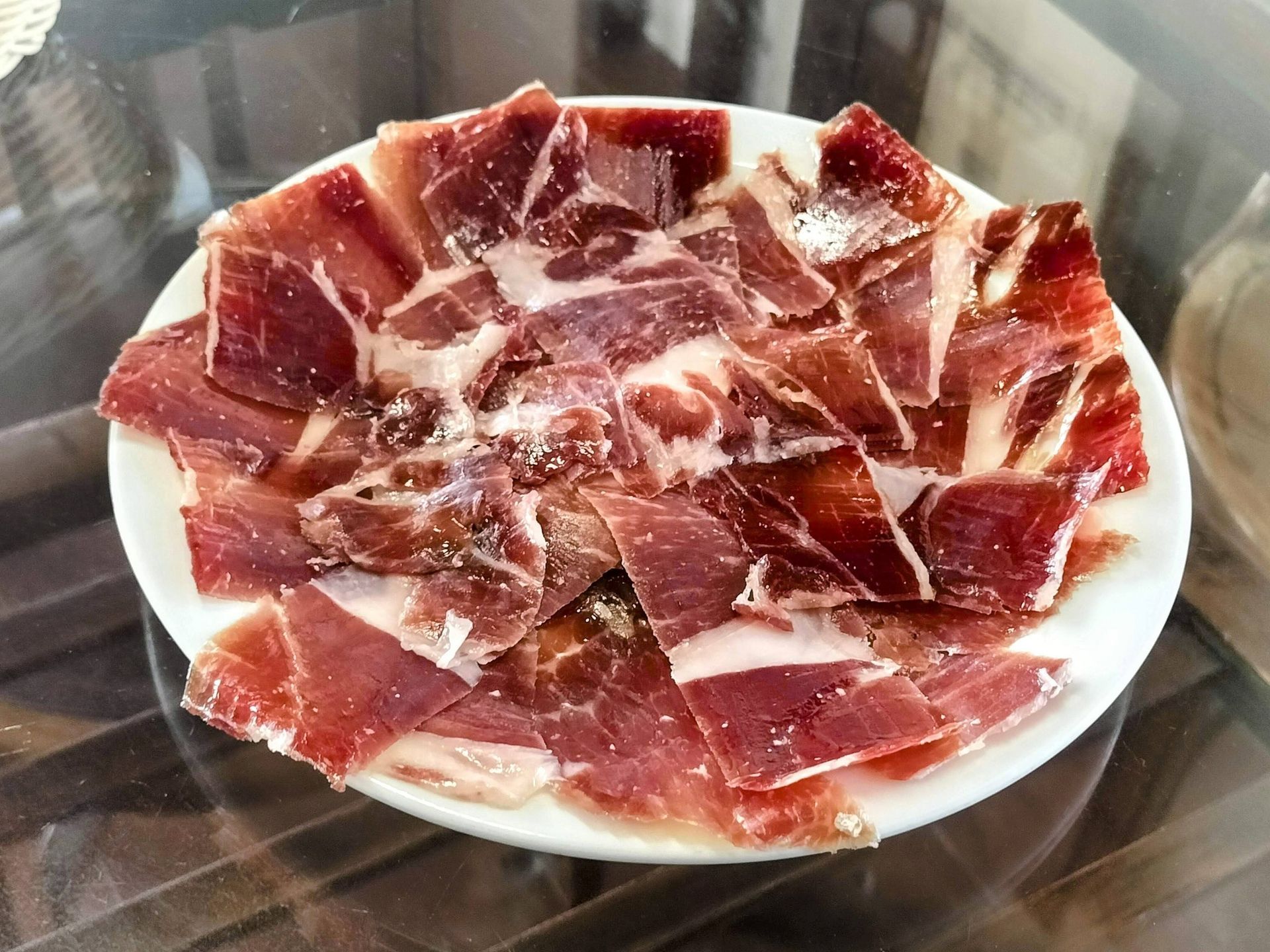 Un plato de jamón ibérico cortado en lonchas finas, de color rosa rojizo con vetas de grasa, espolvoreado con sal.
