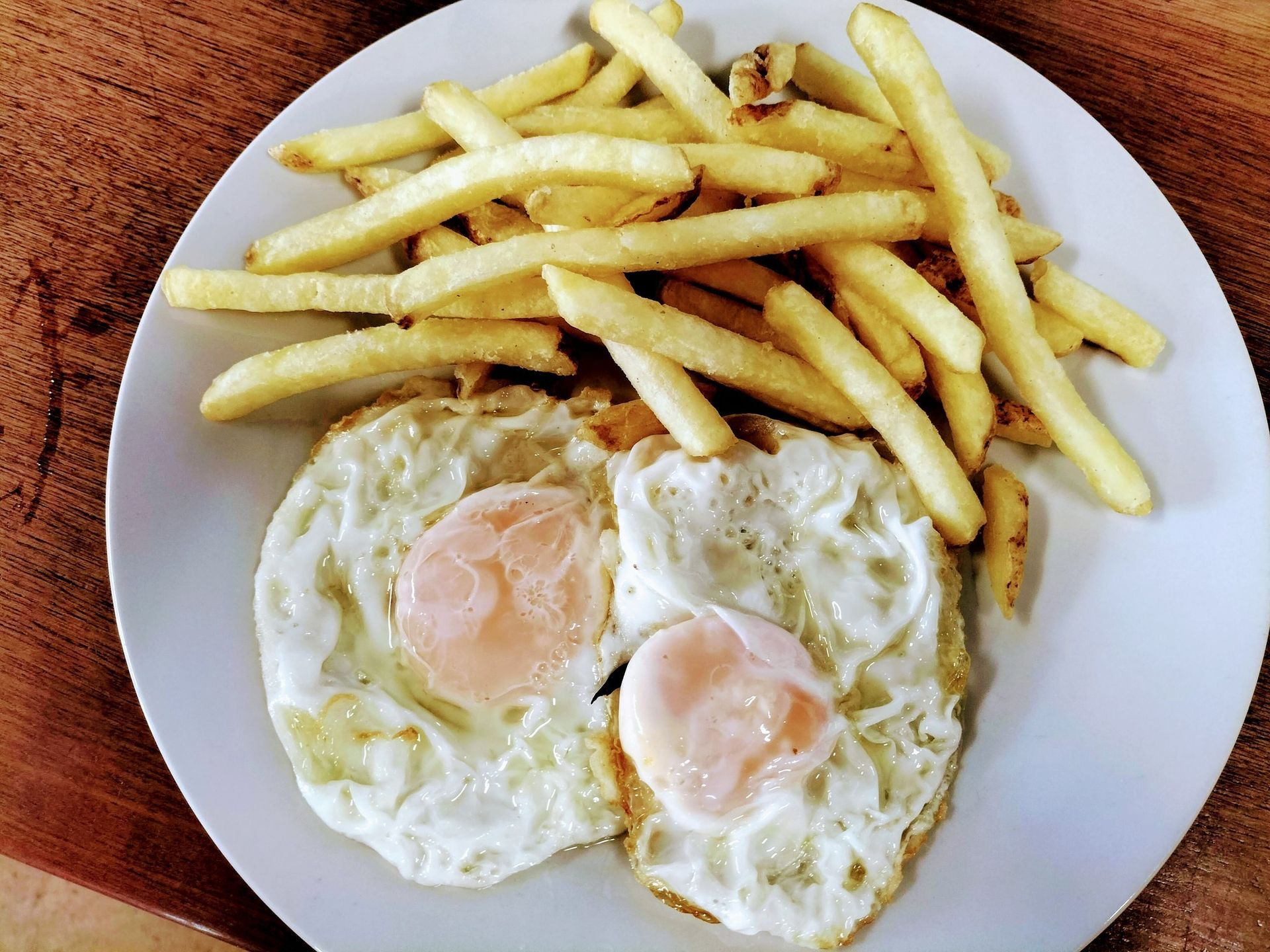 Plato de huevos fritos con yemas líquidas y patatas fritas.