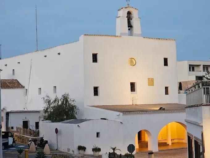 Iglesia blanca con entrada arqueada y campanario, contra un cielo crepuscular.