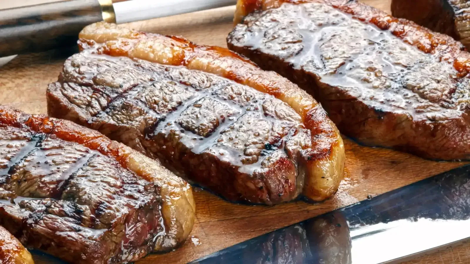 Filetes de picanha a la parrilla sobre una tabla de servir de madera, que muestran una costra marrón y marcas de parrilla.