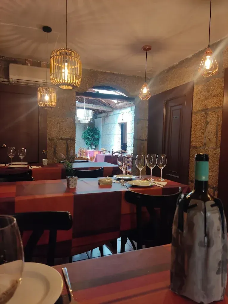 Interior de restaurante con mesas y sillas de madera, paredes de piedra y suelo de baldosas.