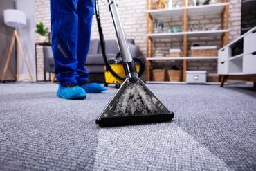 Reinigungskraft saugt einen Teppich mit einem Staubsauger