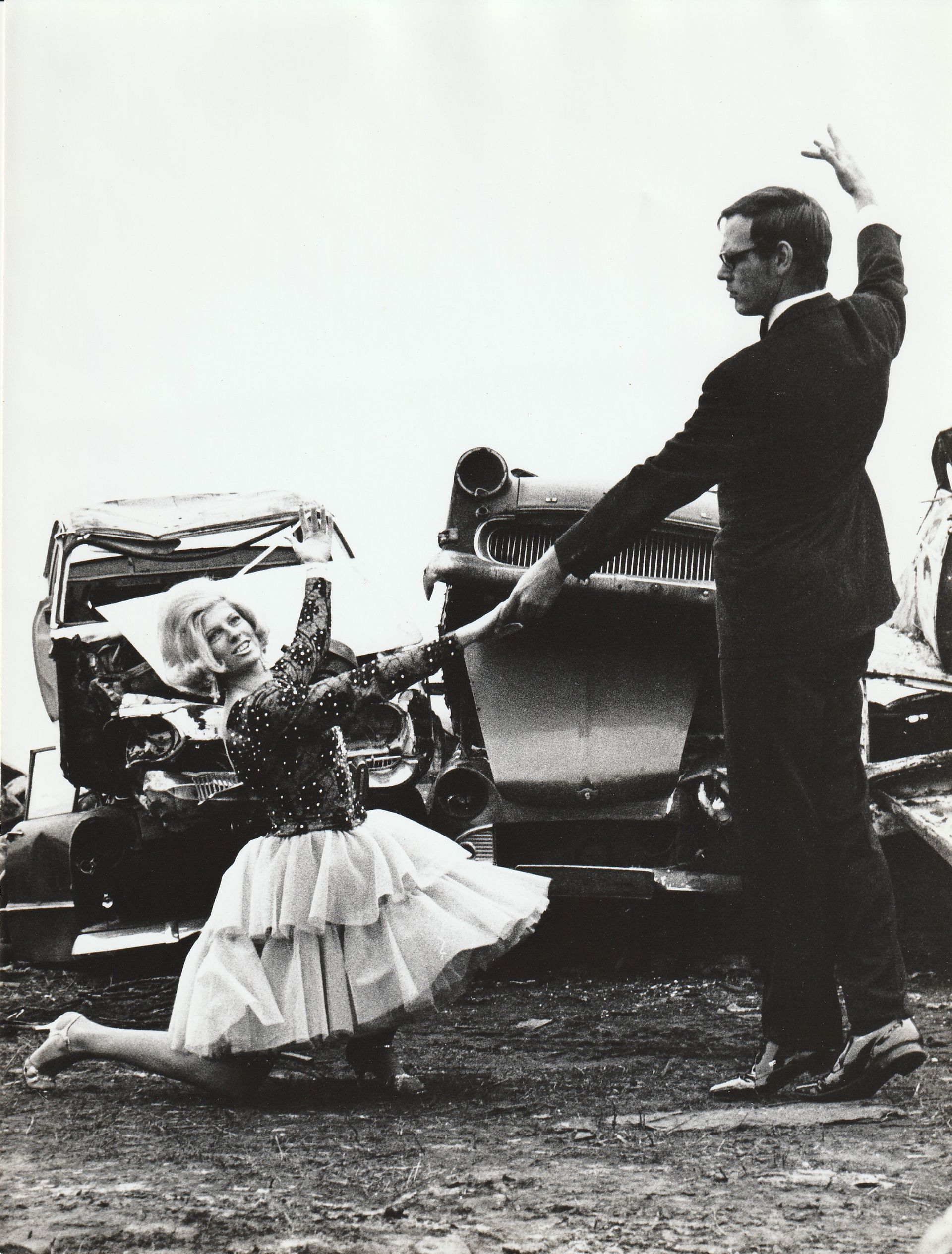 Ein Schwarzweißfoto von einem Mann und einer Frau, die vor einem Auto tanzen